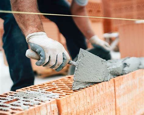 Bricklayer applying mortar to red bricks